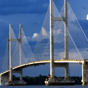 Ponte estaiada em construção com torres de concreto, cabos estruturais e vão sobre área fluvial