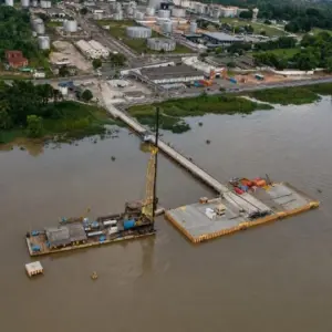Vista aérea de terminal portuário com cais, fundações em ambiente fluvial e área industrial ao fundo