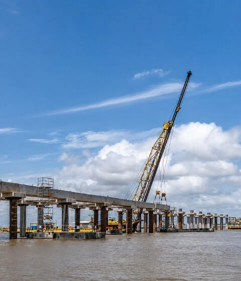 Obra portuária e fluvial com ponte em construção, fundações sobre água e guindaste em operação pela Probase.